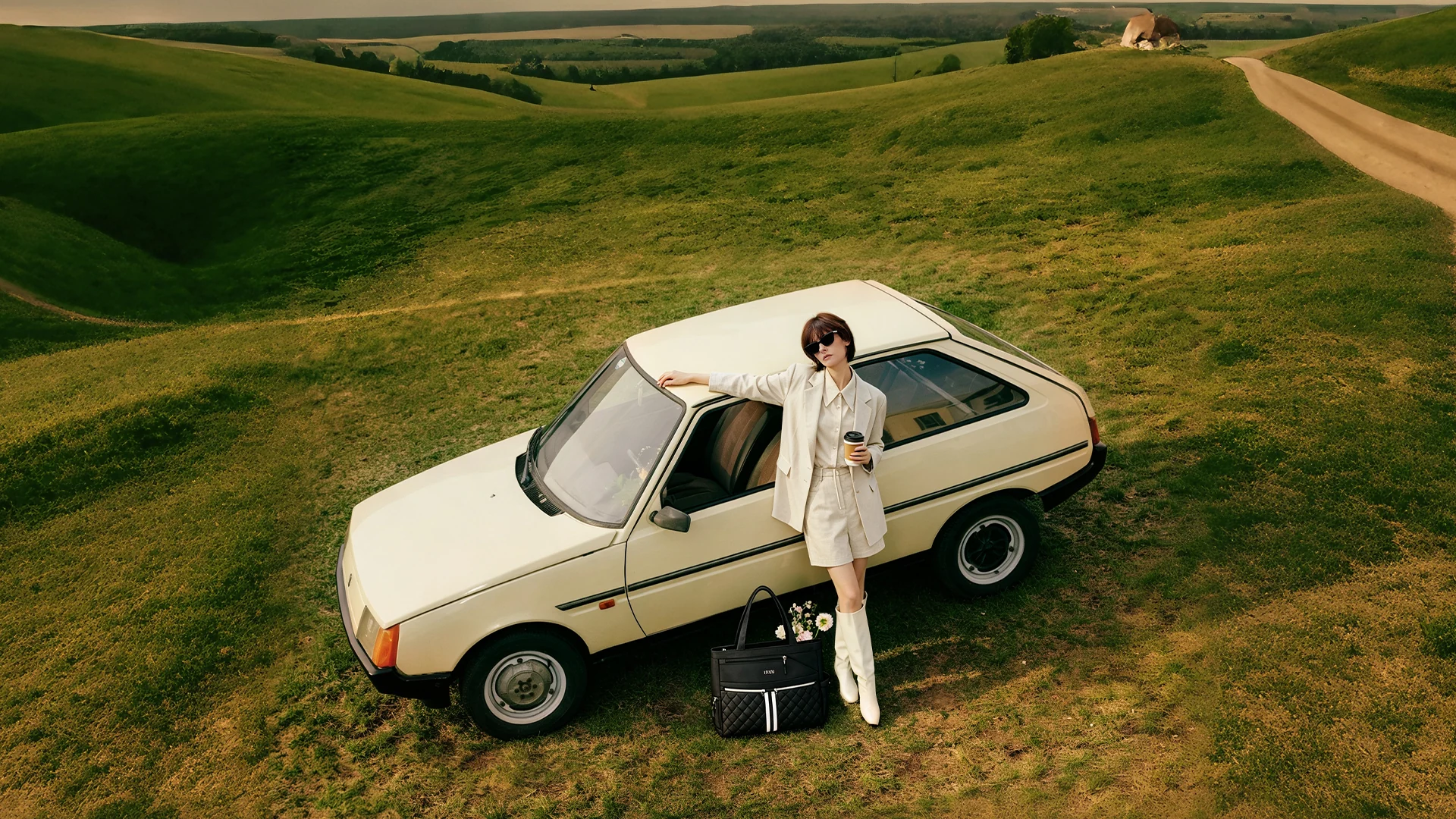 An NST tote beside a traveler and a cream-colored car among rolling green hills.
