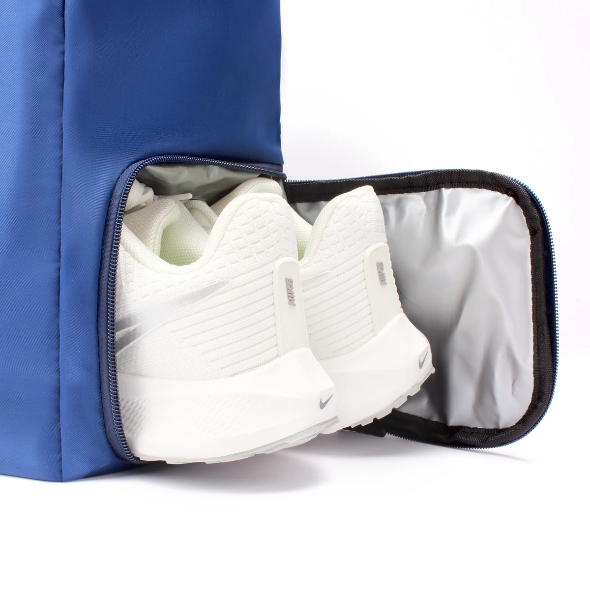 Close-up of the blue NST Tennis Tote's separate lower shoe compartment holding a pair of white athletic shoes.